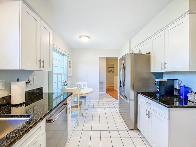 kitchen featuring light tile patterned floors, stainless steel appliances, white cabinetry, and dark stone counters