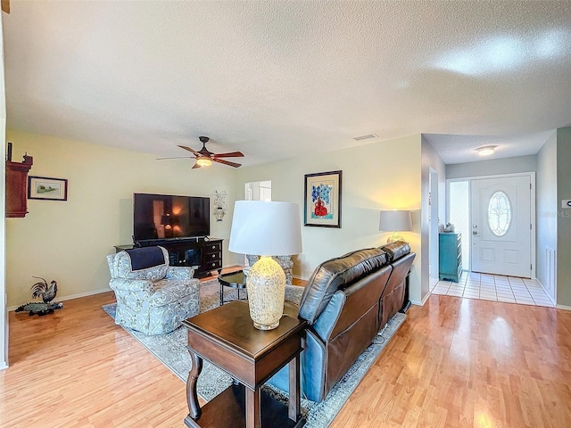 living room with ceiling fan, light hardwood / wood-style floors, and a textured ceiling