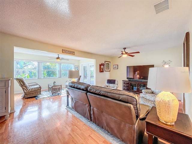 living room with ceiling fan, a textured ceiling, and light wood-type flooring