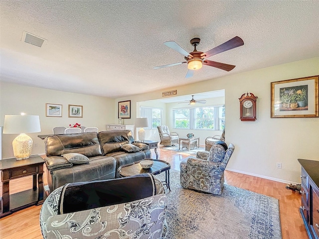 living room featuring ceiling fan, a textured ceiling, and light wood-type flooring