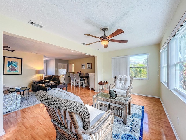 living room featuring a textured ceiling, light hardwood / wood-style flooring, and ceiling fan