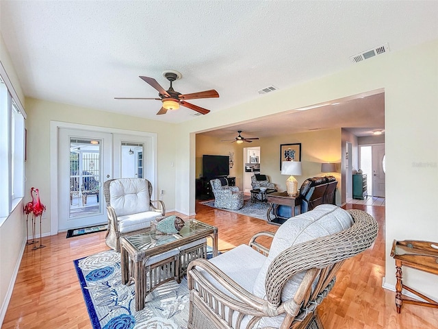 living room featuring french doors, light wood-type flooring, a textured ceiling, and ceiling fan