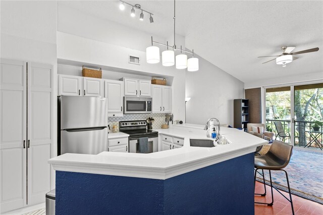 kitchen featuring white cabinets, sink, appliances with stainless steel finishes, decorative light fixtures, and a breakfast bar area