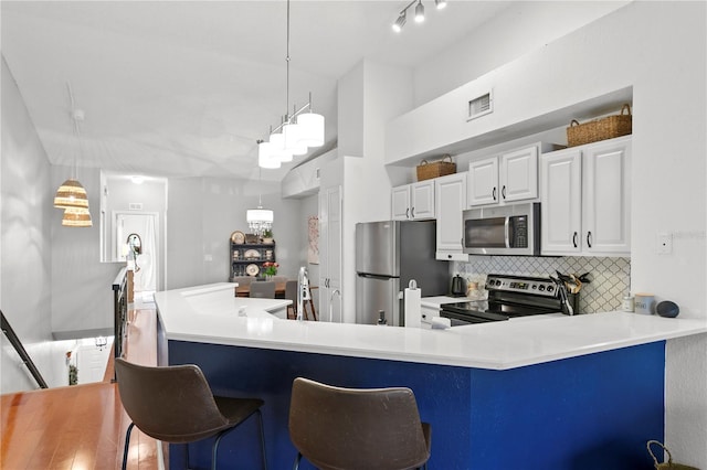 kitchen with backsplash, white cabinets, hanging light fixtures, and appliances with stainless steel finishes