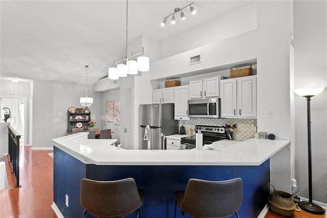 kitchen with kitchen peninsula, white cabinetry, hanging light fixtures, and appliances with stainless steel finishes