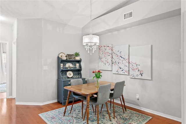 dining area featuring hardwood / wood-style floors, an inviting chandelier, and lofted ceiling