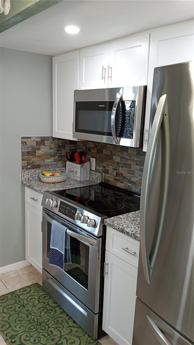 kitchen with appliances with stainless steel finishes, backsplash, light stone counters, white cabinets, and light tile patterned flooring