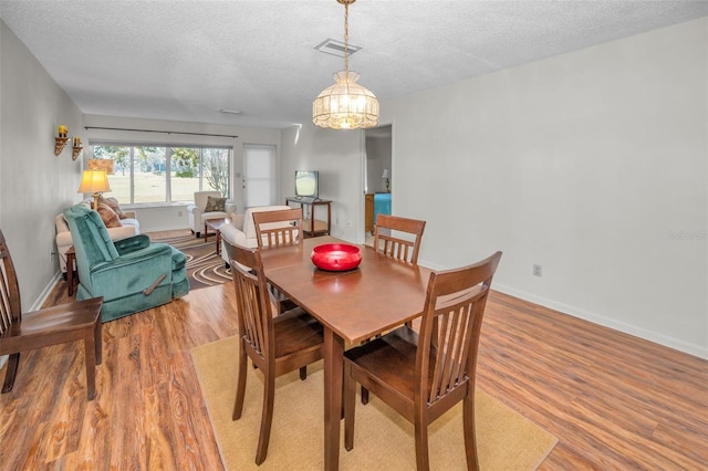 dining room featuring a textured ceiling, an inviting chandelier, and light hardwood / wood-style flooring