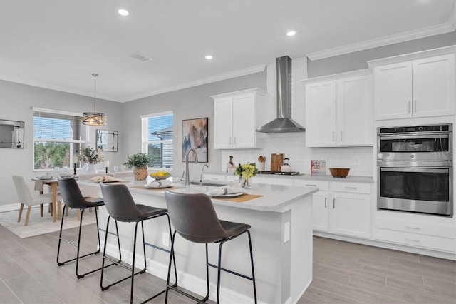 kitchen featuring a kitchen island with sink, white cabinets, wall chimney range hood, sink, and stainless steel appliances