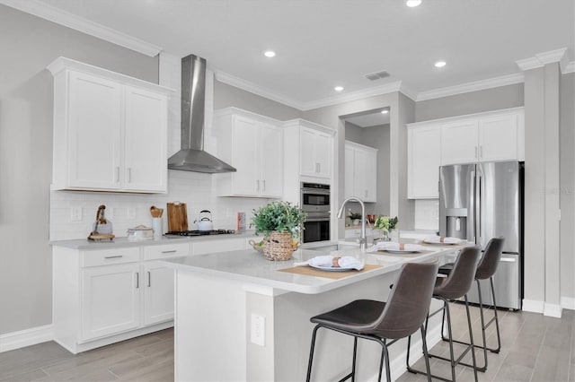 kitchen with a center island with sink, white cabinets, wall chimney exhaust hood, appliances with stainless steel finishes, and a breakfast bar area