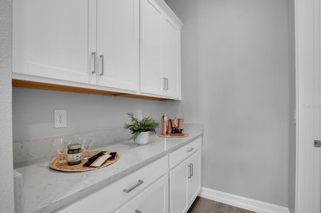 bar featuring light stone counters and white cabinetry