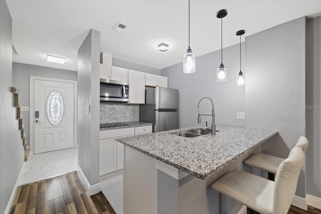 kitchen featuring sink, light stone counters, decorative light fixtures, white cabinets, and appliances with stainless steel finishes