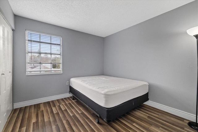 bedroom with a textured ceiling, dark hardwood / wood-style flooring, and a closet