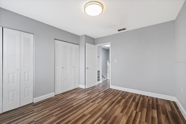 unfurnished bedroom with multiple closets, dark wood-type flooring, and a textured ceiling