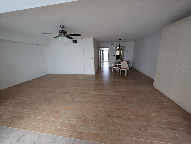 empty room featuring a textured ceiling, ceiling fan with notable chandelier, and light hardwood / wood-style floors