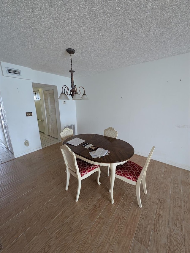 dining room with a textured ceiling, a chandelier, and light hardwood / wood-style flooring