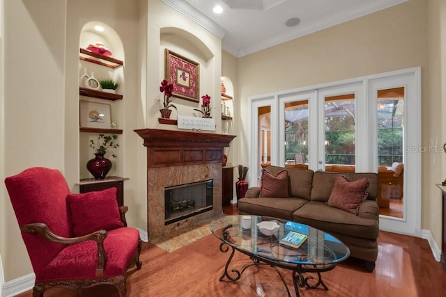 living room featuring built in shelves, a high end fireplace, light wood-type flooring, and ornamental molding