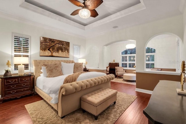 bedroom with a tray ceiling, ceiling fan, dark wood-type flooring, and ornamental molding