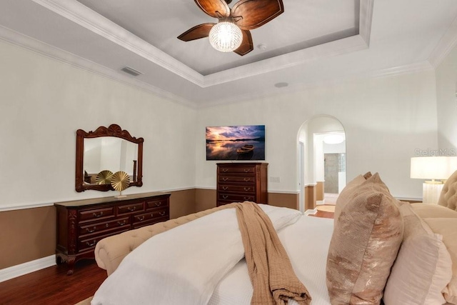 bedroom featuring dark hardwood / wood-style flooring, ensuite bath, ornamental molding, a raised ceiling, and ceiling fan