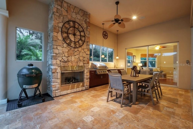 dining area with a towering ceiling, a stone fireplace, and ceiling fan