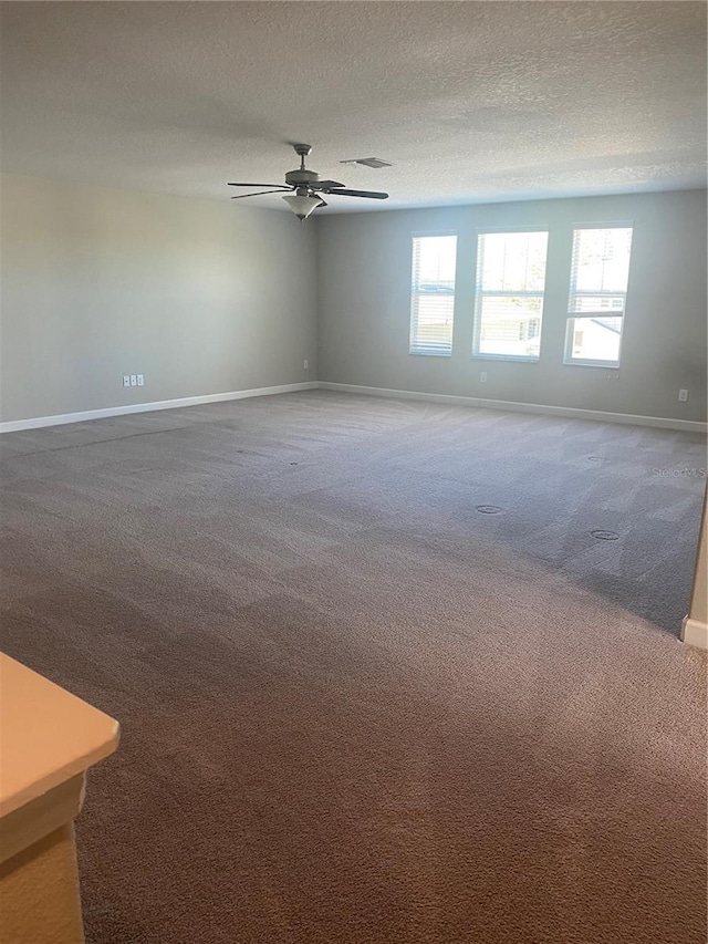 carpeted empty room with visible vents, ceiling fan, a textured ceiling, and baseboards