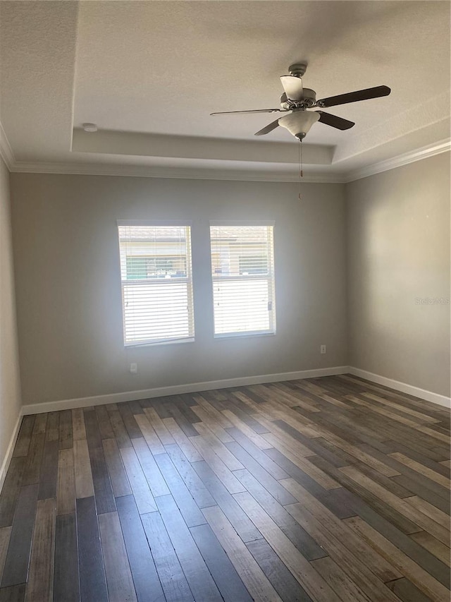 spare room with baseboards, a ceiling fan, dark wood-type flooring, a tray ceiling, and crown molding