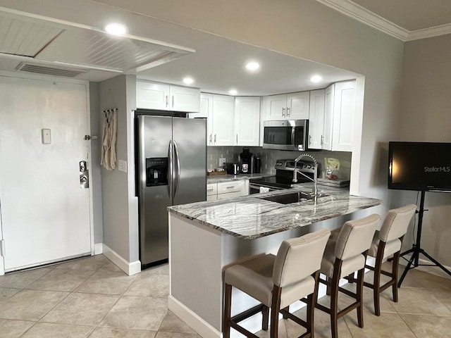 kitchen with sink, white cabinetry, light stone counters, appliances with stainless steel finishes, and kitchen peninsula