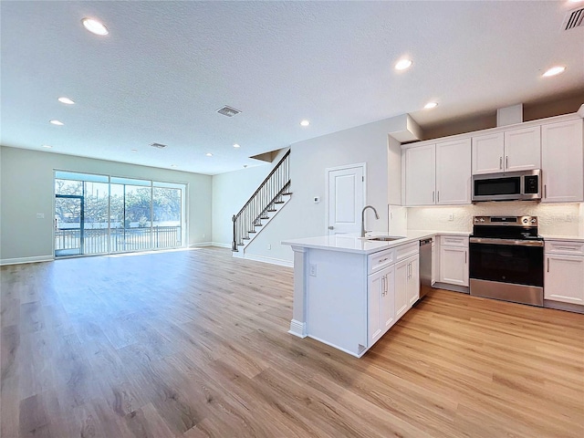 kitchen with white cabinets, sink, light hardwood / wood-style flooring, kitchen peninsula, and stainless steel appliances