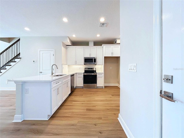 kitchen with sink, stainless steel appliances, kitchen peninsula, white cabinets, and light wood-type flooring