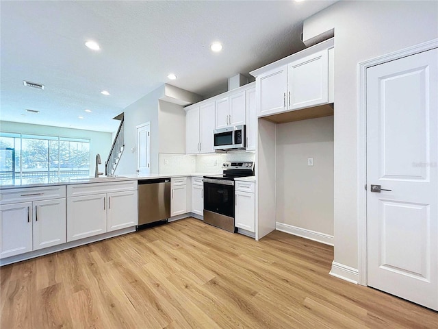 kitchen with white cabinets, light wood-type flooring, stainless steel appliances, and sink