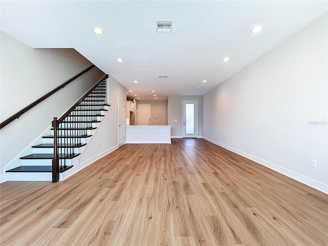 unfurnished living room with a textured ceiling and light hardwood / wood-style floors