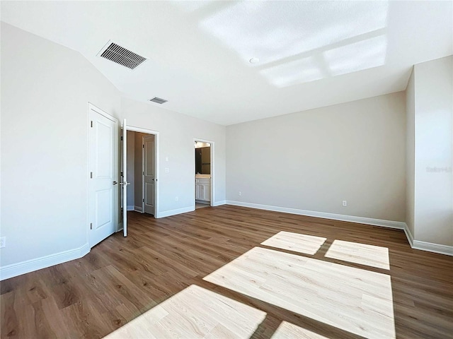 unfurnished bedroom featuring ensuite bathroom, dark hardwood / wood-style floors, and vaulted ceiling