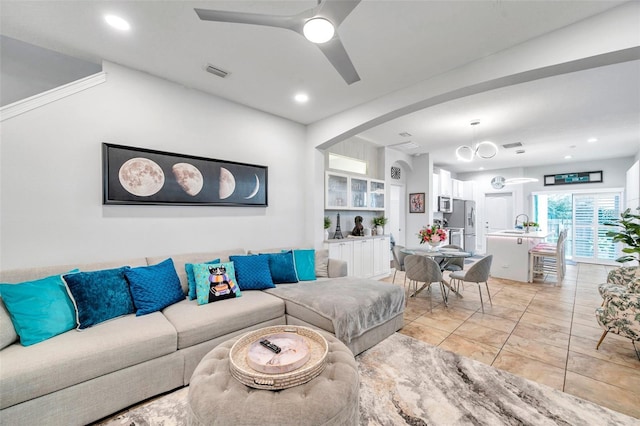 tiled living room with ceiling fan, built in features, and sink