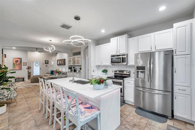 kitchen with a kitchen bar, appliances with stainless steel finishes, a kitchen island with sink, ceiling fan, and hanging light fixtures