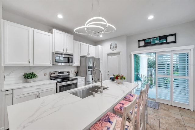 kitchen with appliances with stainless steel finishes, a center island with sink, white cabinetry, and sink