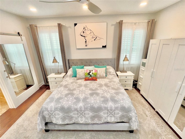 bedroom with a barn door, ceiling fan, and light hardwood / wood-style flooring