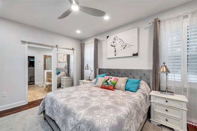 bedroom featuring a barn door, ceiling fan, and light wood-type flooring