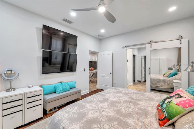 bedroom featuring a barn door, light hardwood / wood-style floors, and ceiling fan