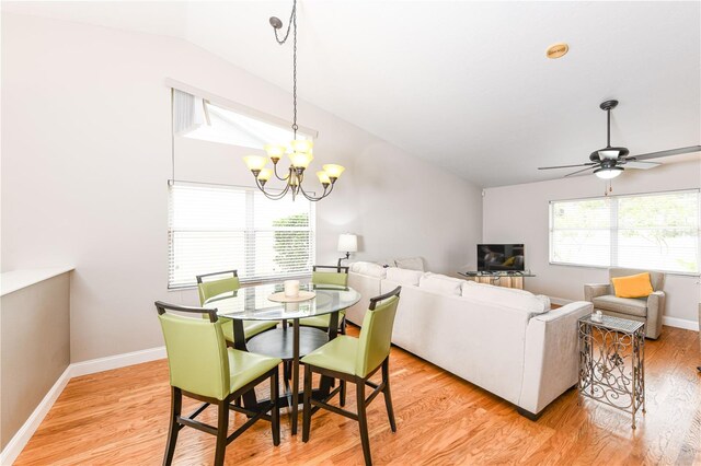 dining space with ceiling fan with notable chandelier, light hardwood / wood-style flooring, and vaulted ceiling