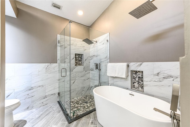 bathroom featuring tile walls, toilet, and plus walk in shower