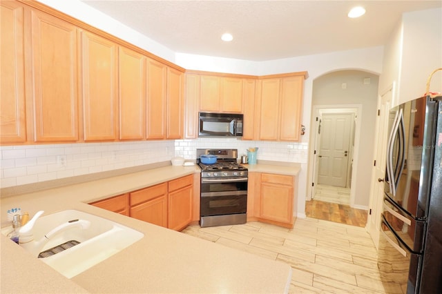 kitchen featuring sink, stainless steel appliances, light brown cabinetry, and tasteful backsplash