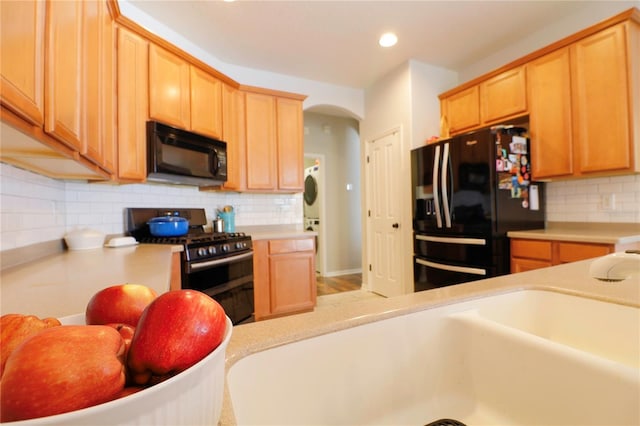 kitchen with decorative backsplash, sink, stacked washer and clothes dryer, and black appliances