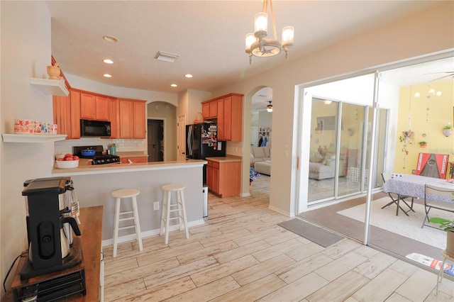 kitchen featuring kitchen peninsula, decorative backsplash, ceiling fan with notable chandelier, black appliances, and a breakfast bar area