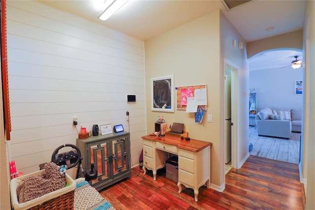 home office with ceiling fan, dark wood-type flooring, and wood walls