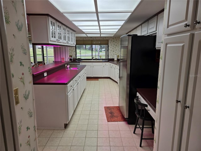 kitchen with stainless steel refrigerator, white cabinets, light tile patterned floors, and sink