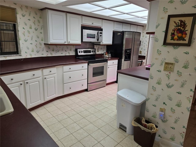 kitchen with white cabinets, appliances with stainless steel finishes, light tile patterned flooring, and a skylight