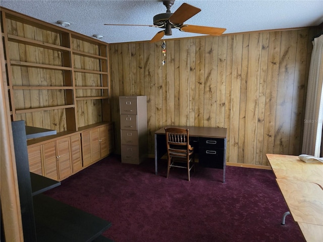 office area featuring a textured ceiling, ceiling fan, wooden walls, and dark colored carpet