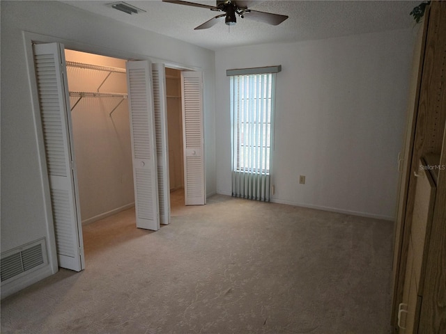 unfurnished bedroom with a textured ceiling, radiator, light colored carpet, two closets, and ceiling fan