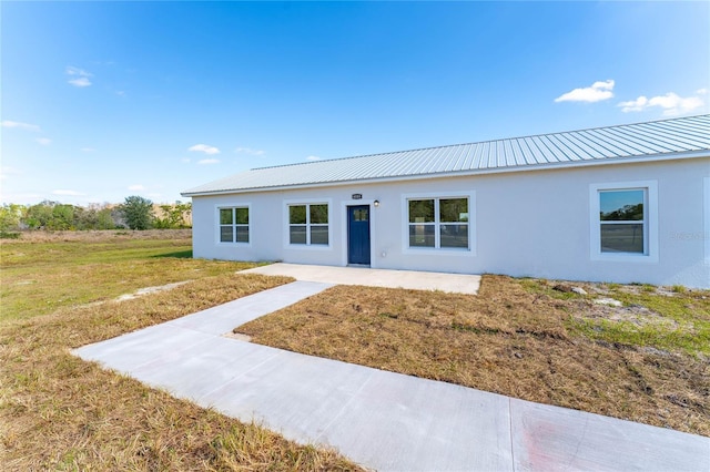 view of front of house with a front yard, a patio area, metal roof, and stucco siding