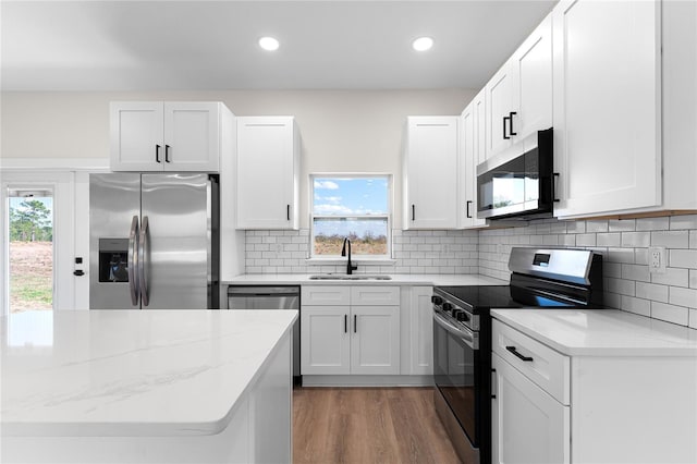 kitchen with light stone counters, light wood finished floors, appliances with stainless steel finishes, white cabinetry, and a sink